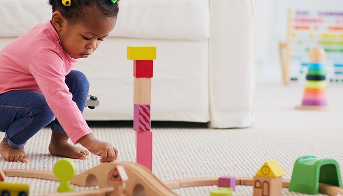 Young toddler girl plays with wooden blocks and a wooden train track set