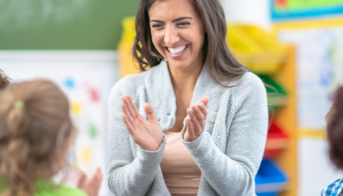 Female teacher smiles and claps with group of young children